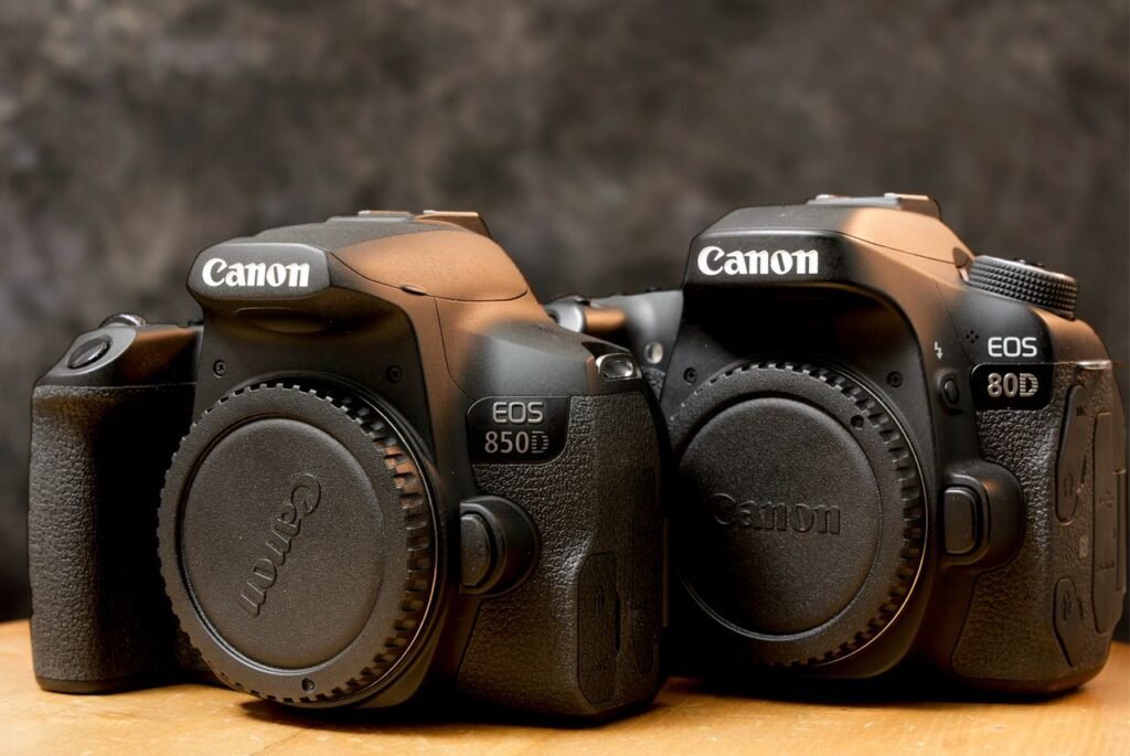 Close-up of two Canon DSLR cameras with lens caps in dim lighting on a wooden table.