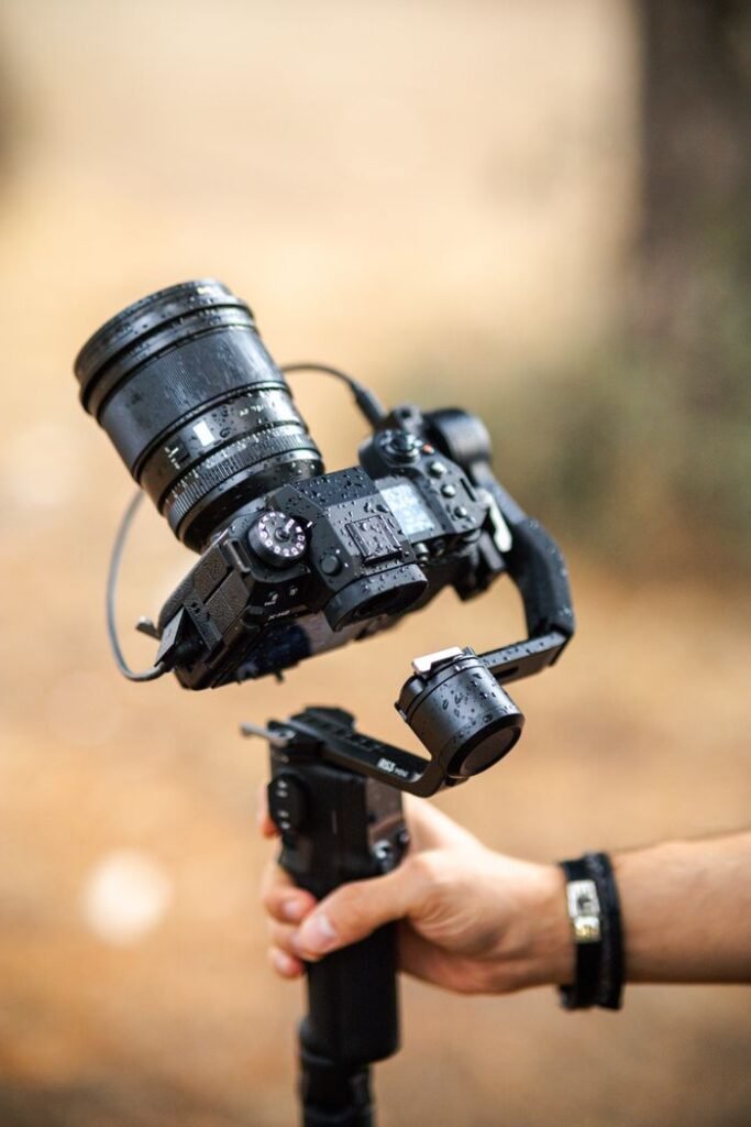 Close-up of a DSLR camera mounted on a gimbal stabilizer held by a person outdoors.