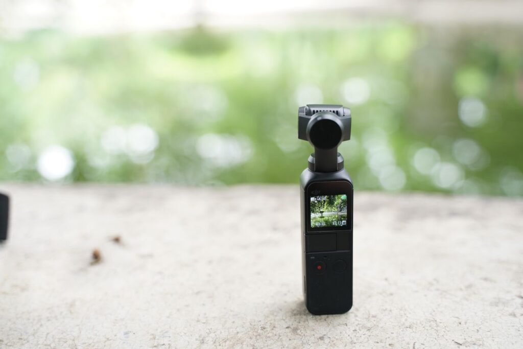 Compact wireless video camera with screen, placed outdoors with blurred natural background.